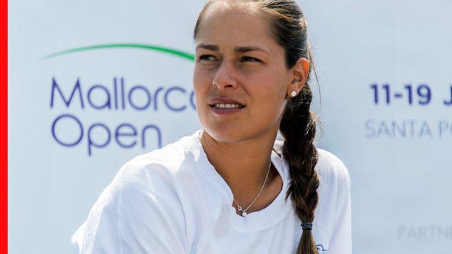 Close-up of a female physiotherapist looking thoughtfully off-camera at a sports event, wearing a white shirt and a side braid with the Mallorca Open banner behind her.