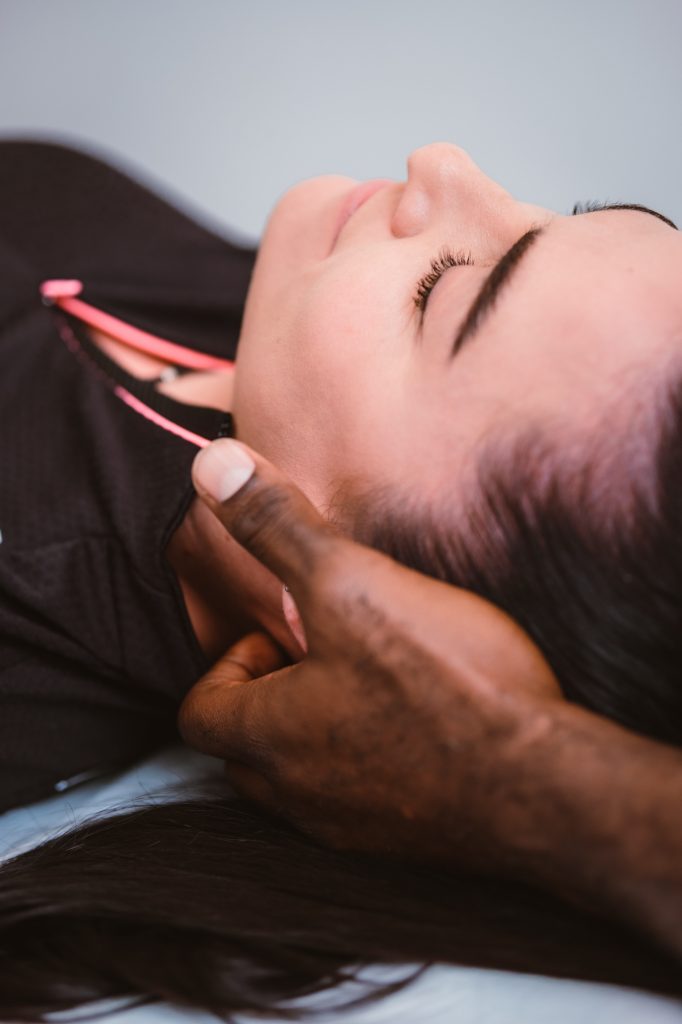 Close-up of a female patient lying down with eyes closed while a male physiotherapist performs a manual neck adjustment and cervical spine massage.