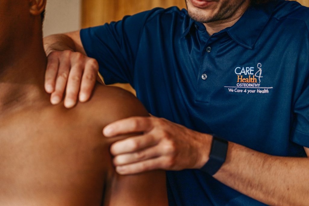 A close-up shot of a specialist at Carefour Health in Mallorca performing a biomechanical assessment and manual palpation of a patient's shoulder and neck muscles.